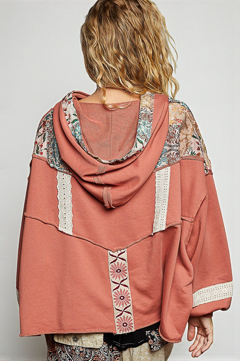 Person wearing a pink hooded jacket with floral patterns on a plain background