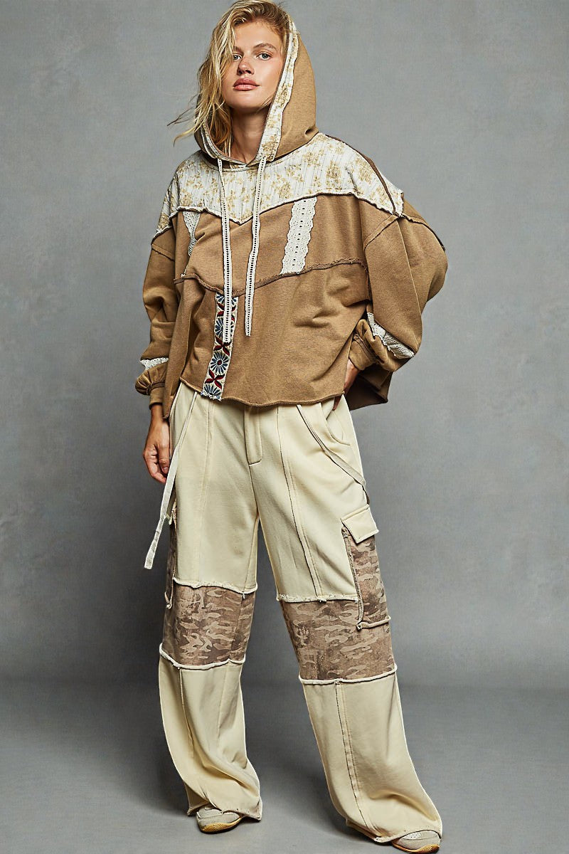 Person wearing a brown and beige outfit with a hood against a gray background