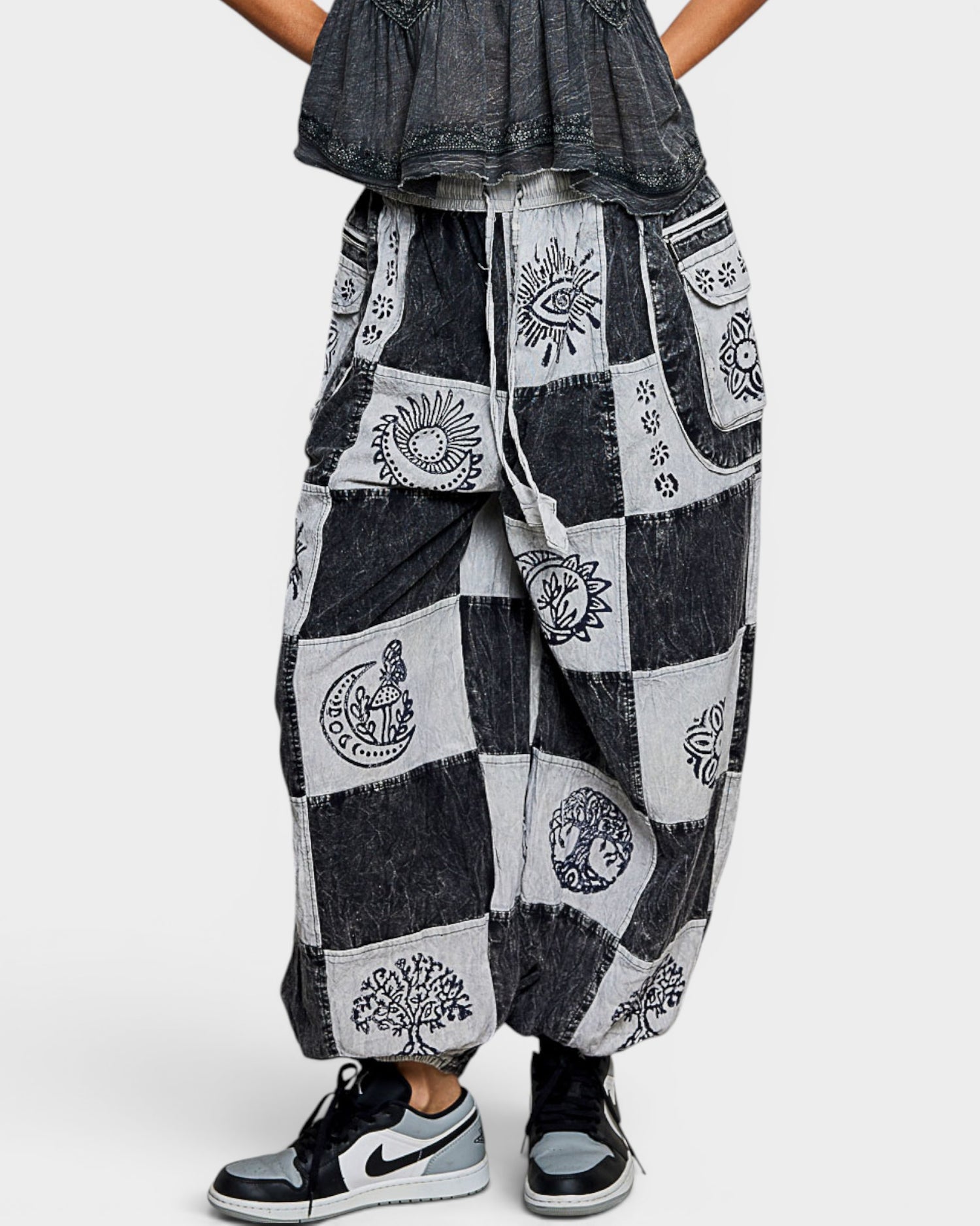 Person wearing a black and white patchwork harem pants with a plain background