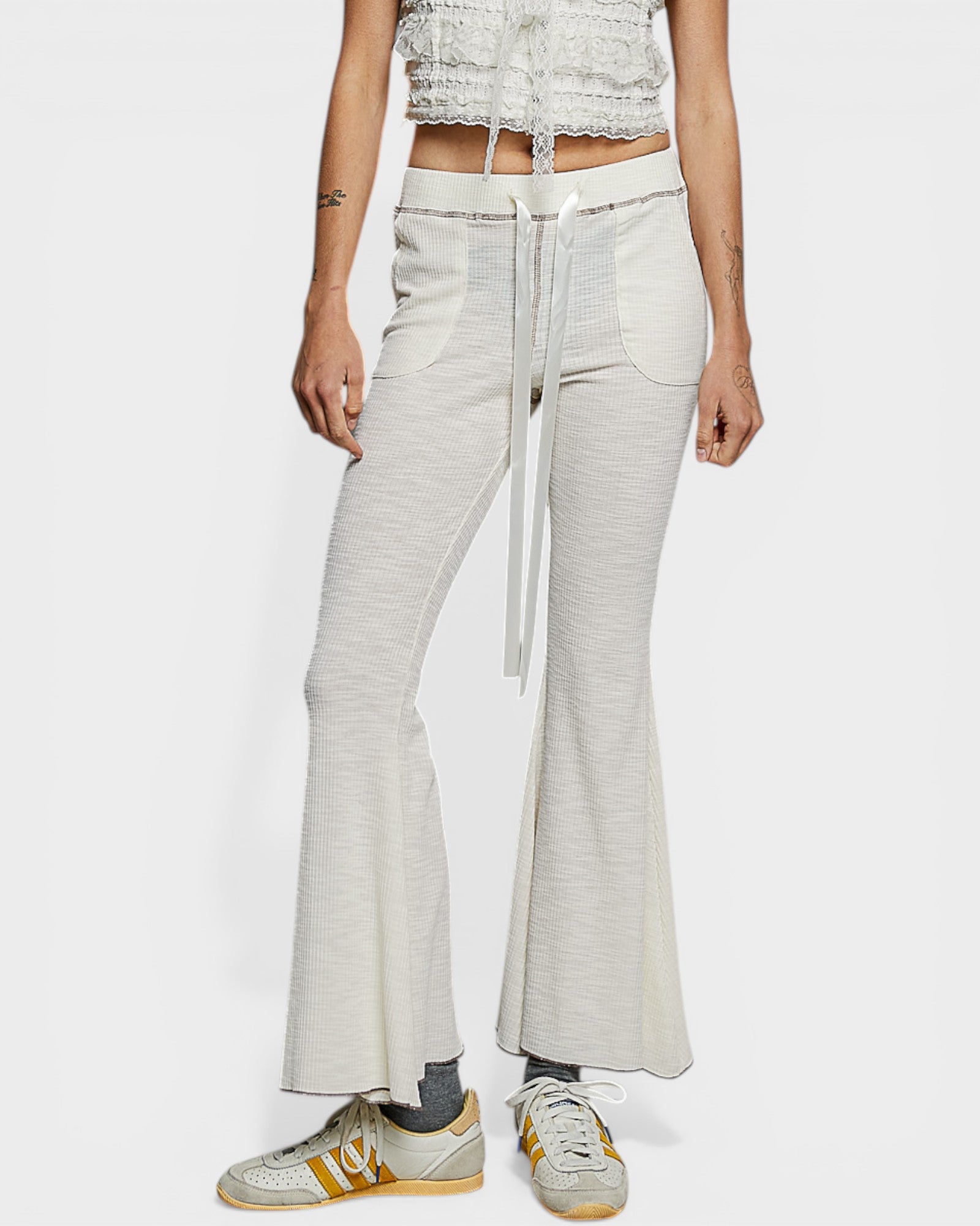 Person wearing light gray flared pants with a white background