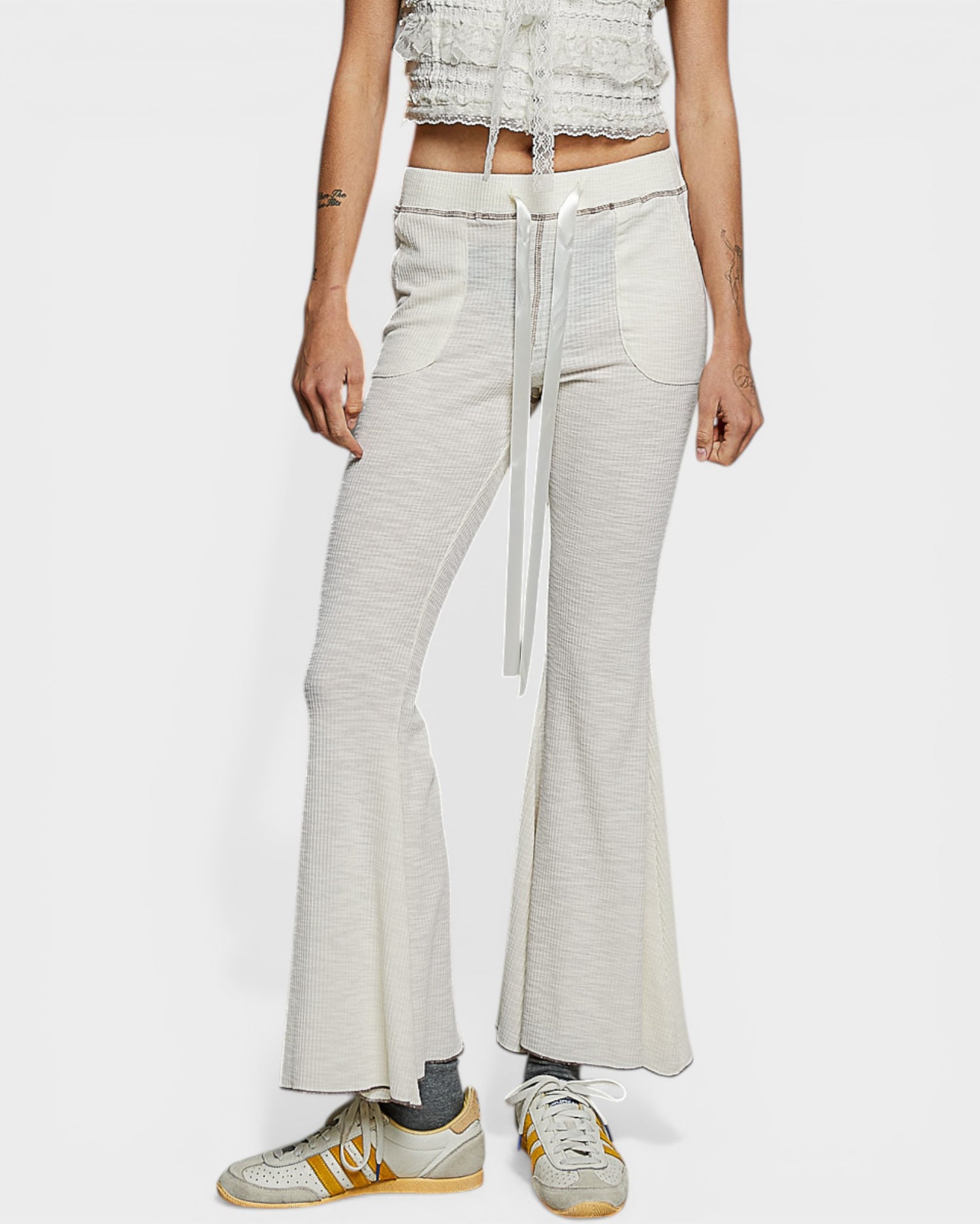 Person wearing light gray flared pants with a white background