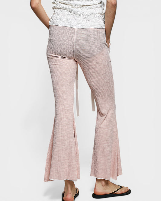 Person wearing light pink flared pants on a white background