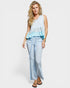 Woman wearing a light blue sleeveless top with ruffled details and light blue jeans on a white background