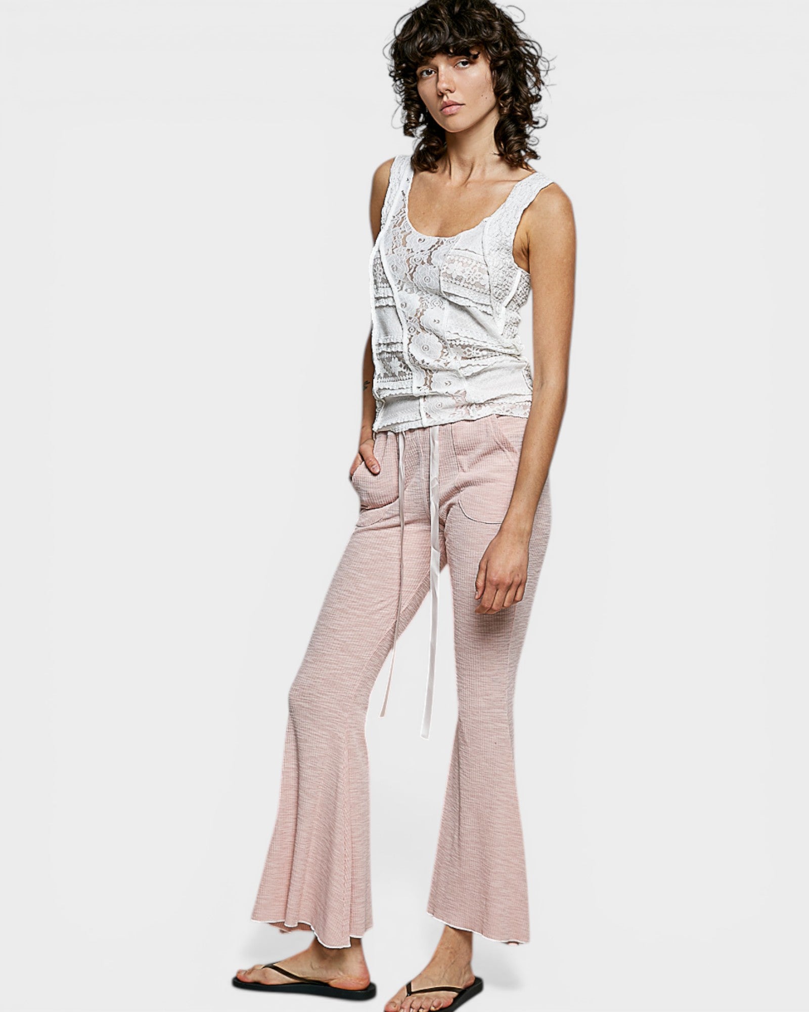 Woman wearing a white sleeveless top and pink pants on a white background
