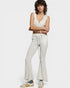 Woman wearing a white lace top and light gray flared pants on a white background