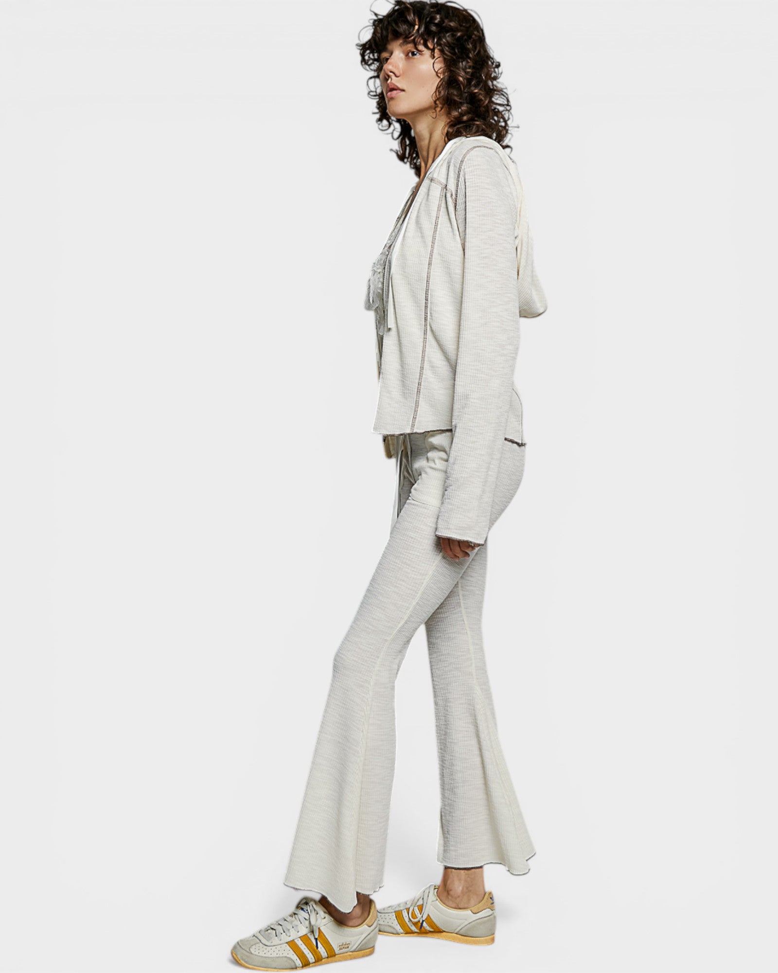 Woman wearing a light gray outfit with flared pants on a white background