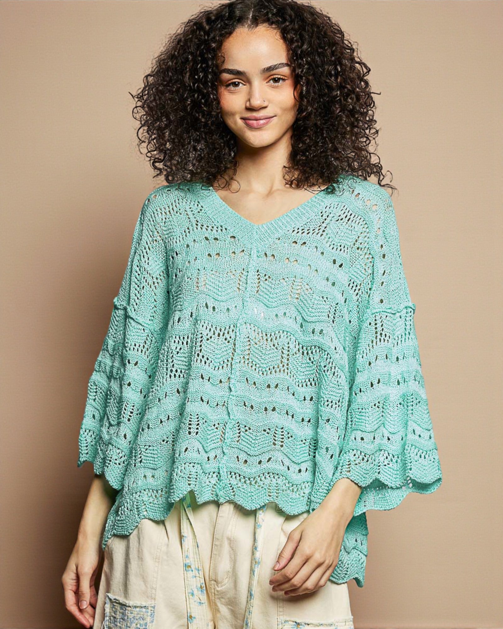 Woman wearing a light blue crochet poncho against a beige background