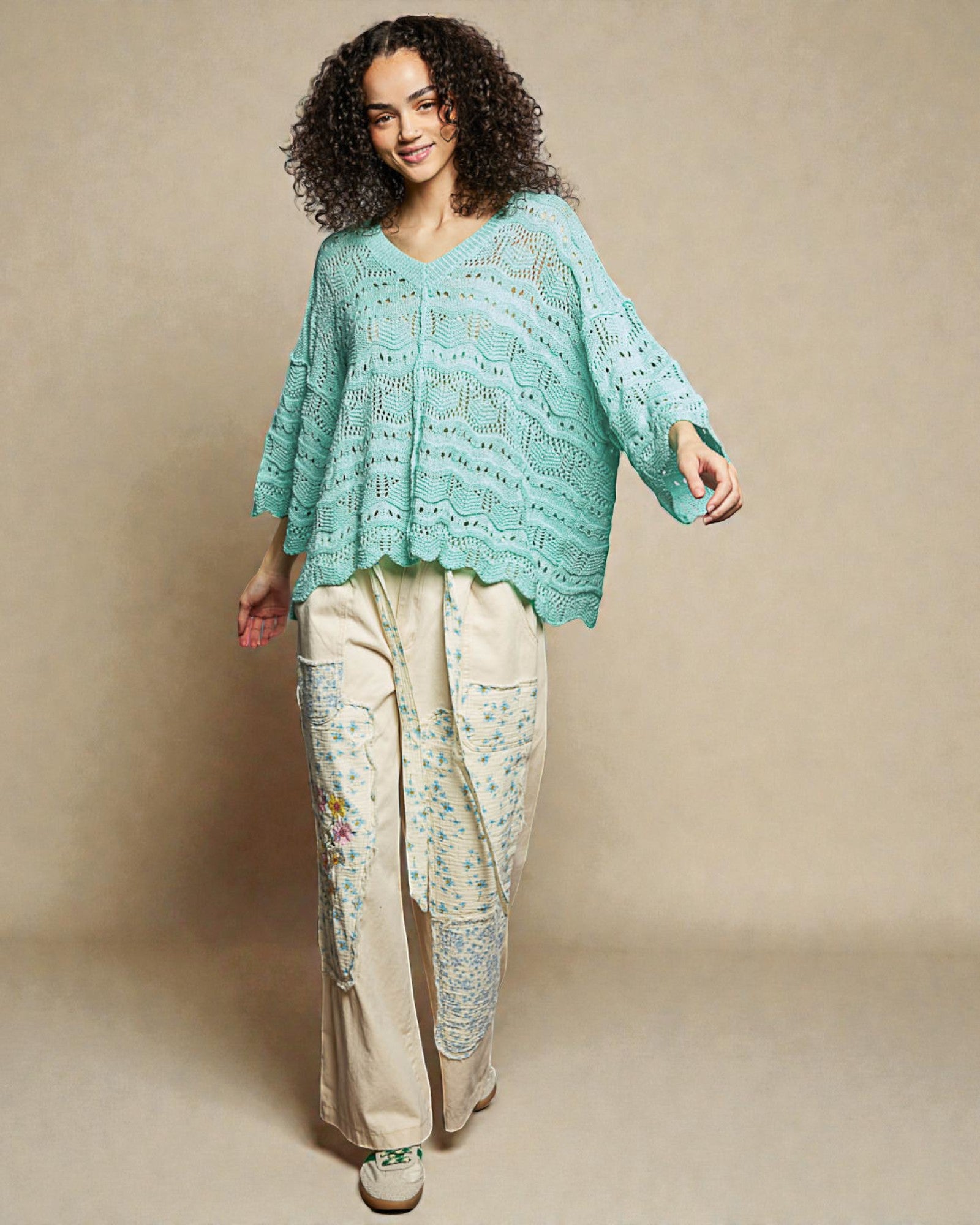 Woman wearing a light blue lace top and beige floral pants against a beige background
