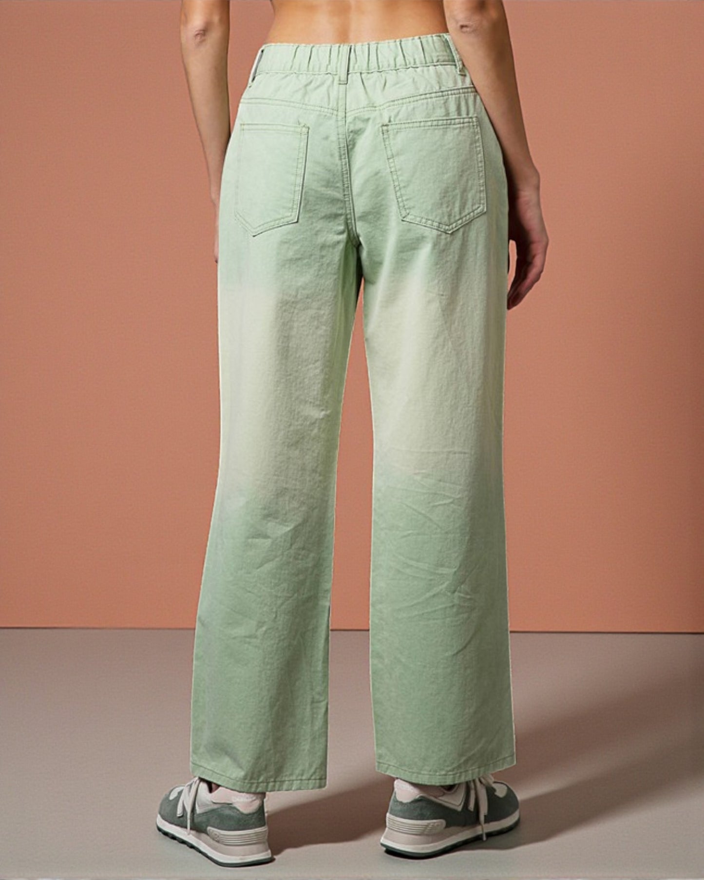 Person wearing light green wide-leg pants against a pink background