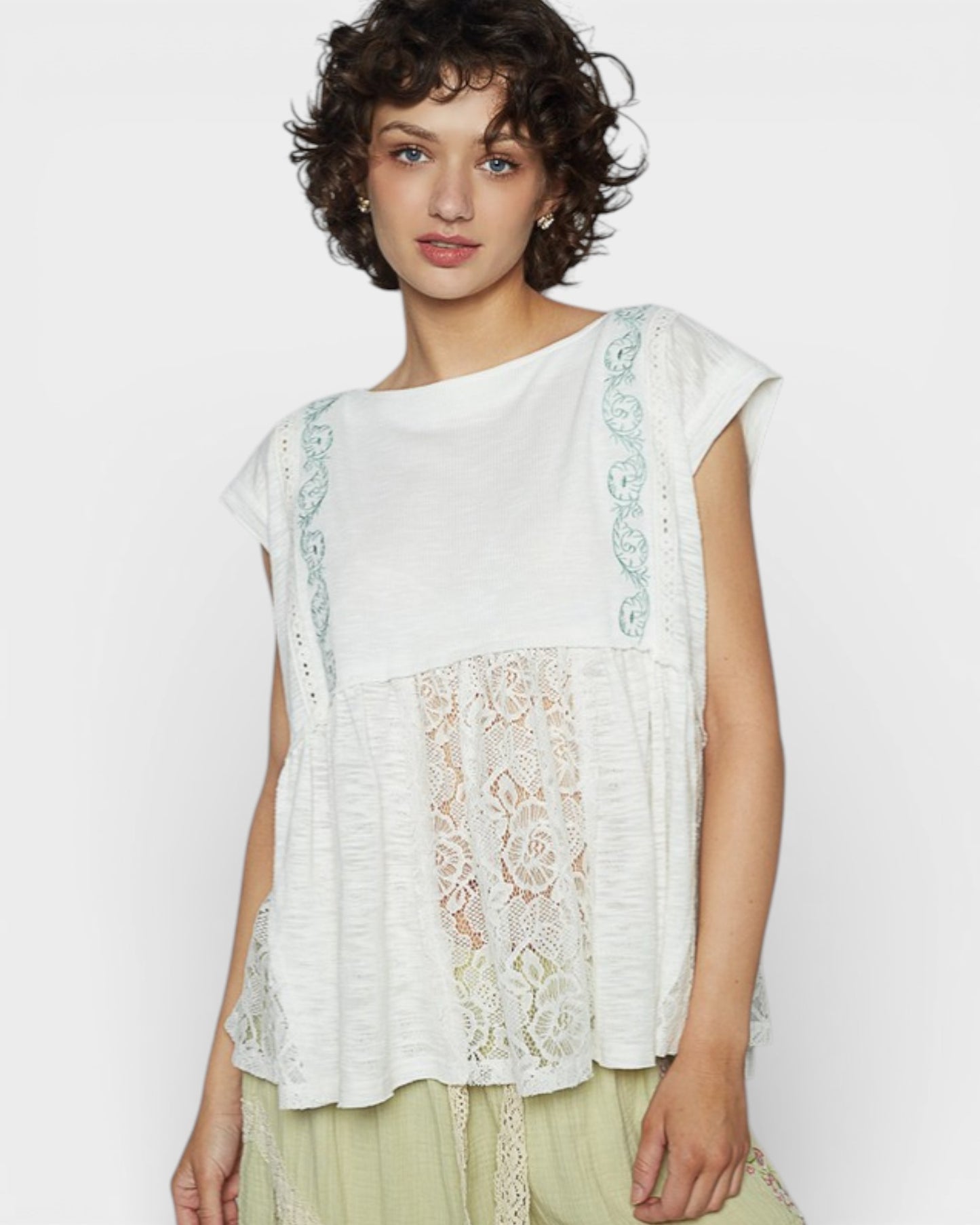 Woman wearing a white top with lace details on a plain background