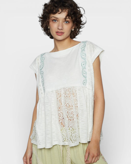 Woman wearing a white top with lace details on a plain background