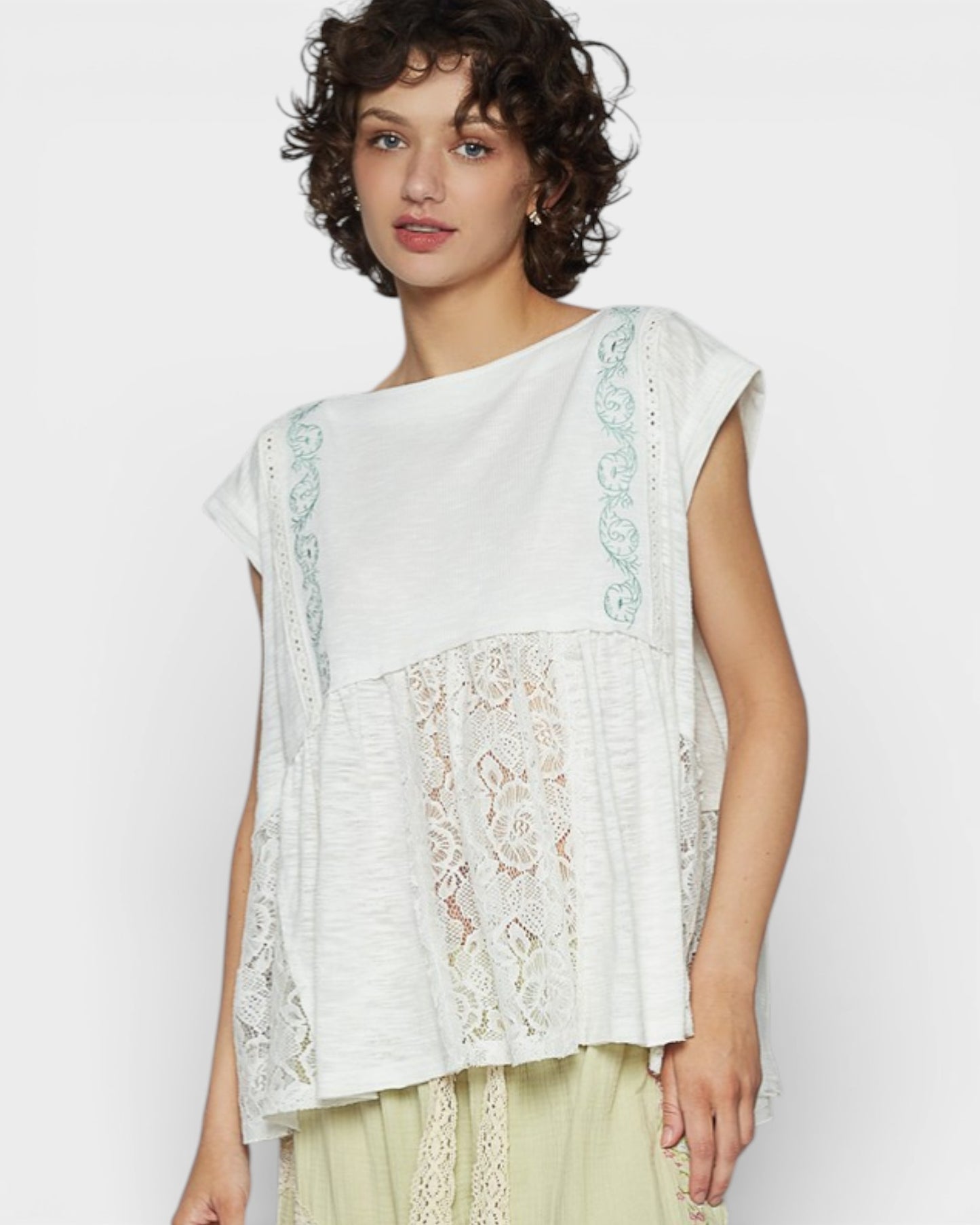 Woman wearing a white sleeveless top with lace details on a plain background