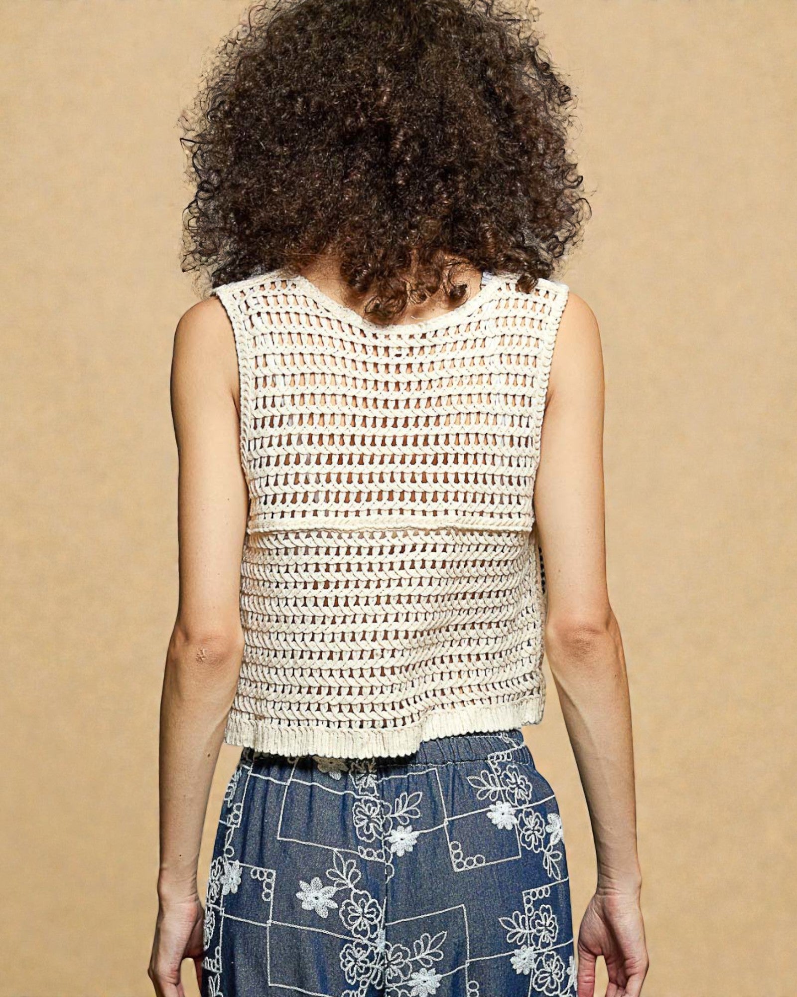 Person wearing a sleeveless crochet top with a beige background