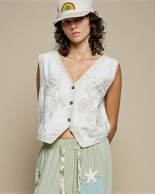 Woman wearing a floral embroidered vest over a light green dress with a plain background