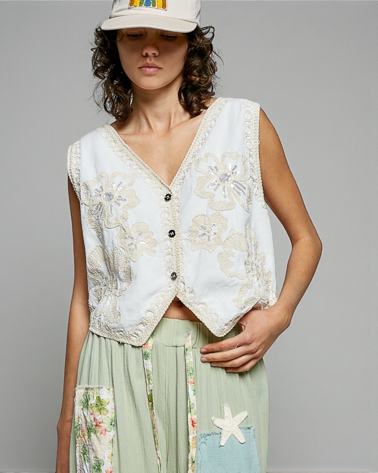 Woman wearing a floral embroidered vest over a dress with a plain background