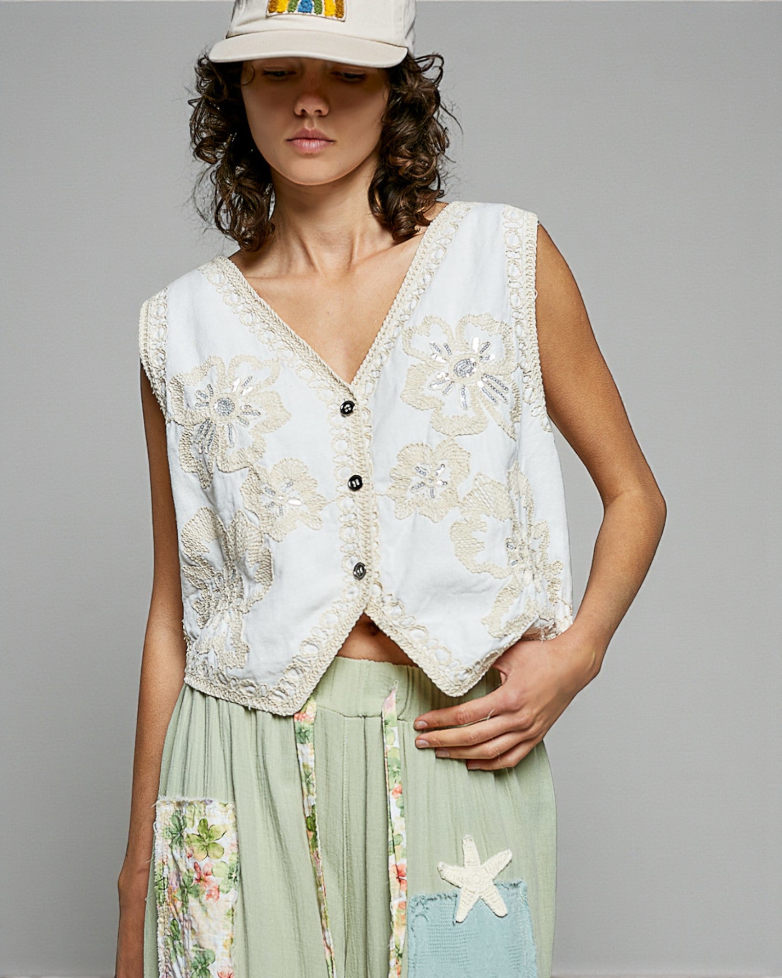 Woman wearing a floral embroidered vest over a dress with a plain background