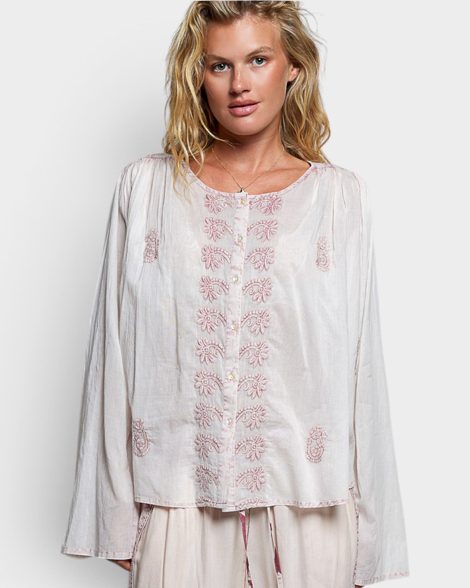 Woman wearing a white embroidered blouse on a plain background