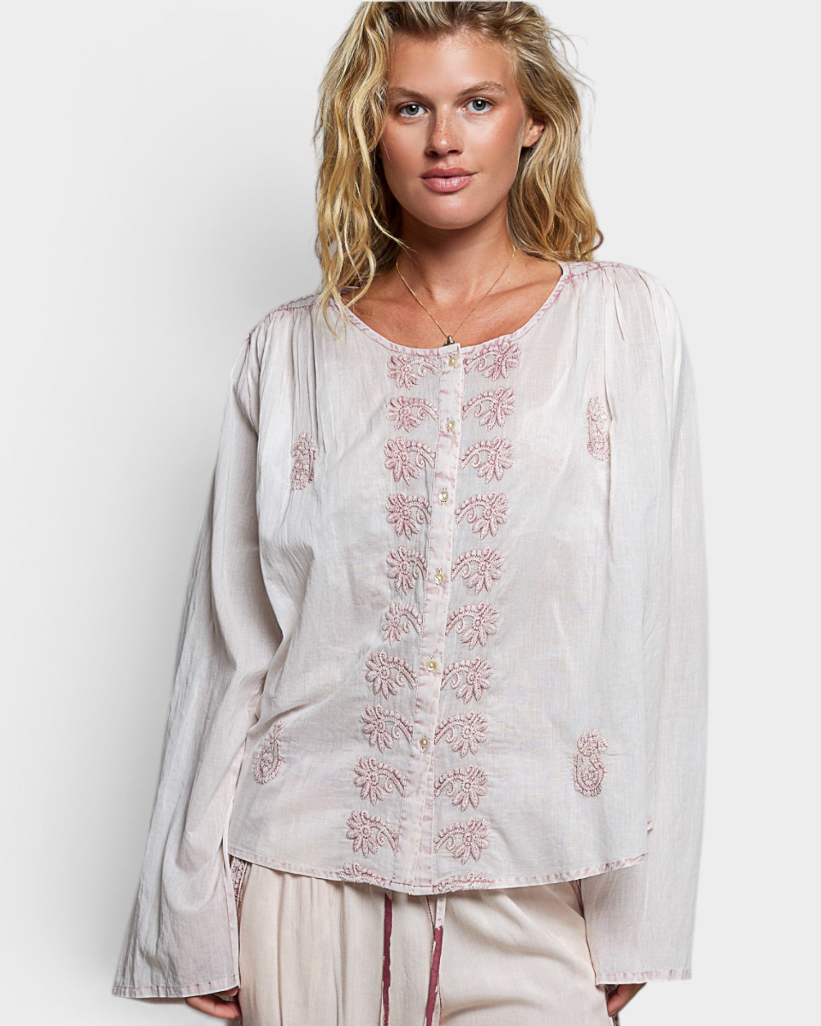 Woman wearing a white blouse with floral embroidery on a plain background