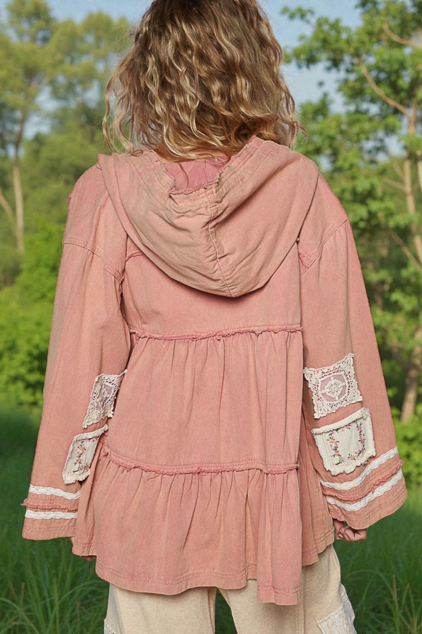 Person wearing a pink hooded jacket with lace details in a natural setting