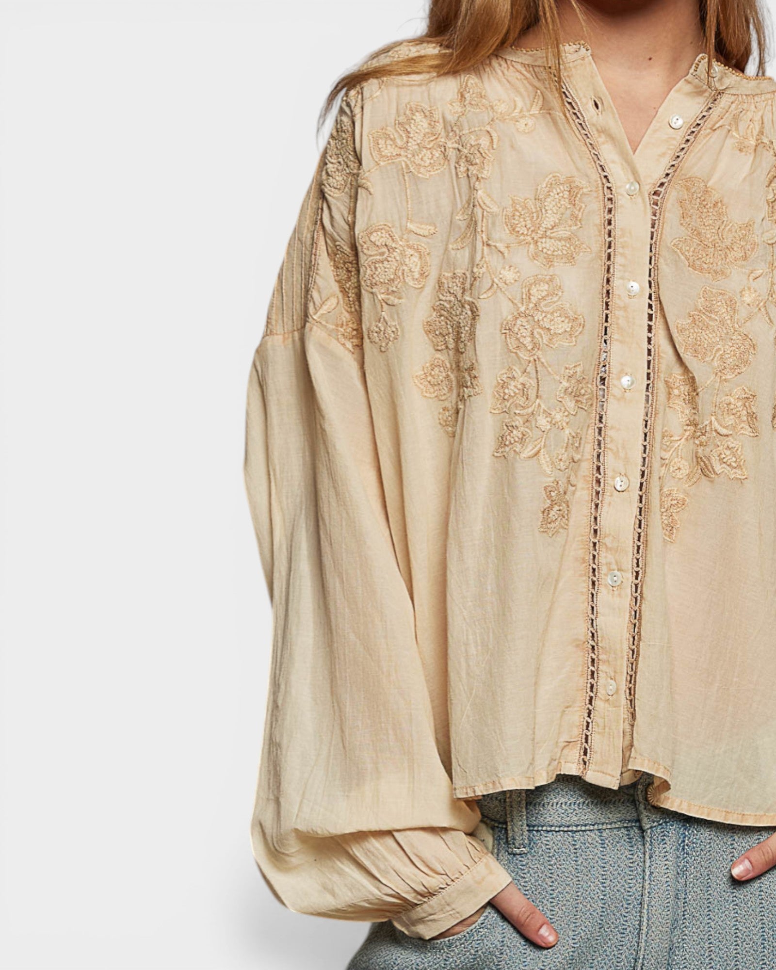 Beige embroidered blouse worn by a person on a white background
