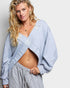 Woman wearing a light blue sweatshirt over a striped outfit on a plain background