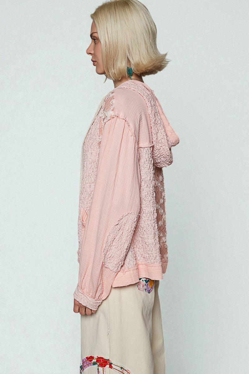 Person wearing a light pink lace top and white pants on a plain background