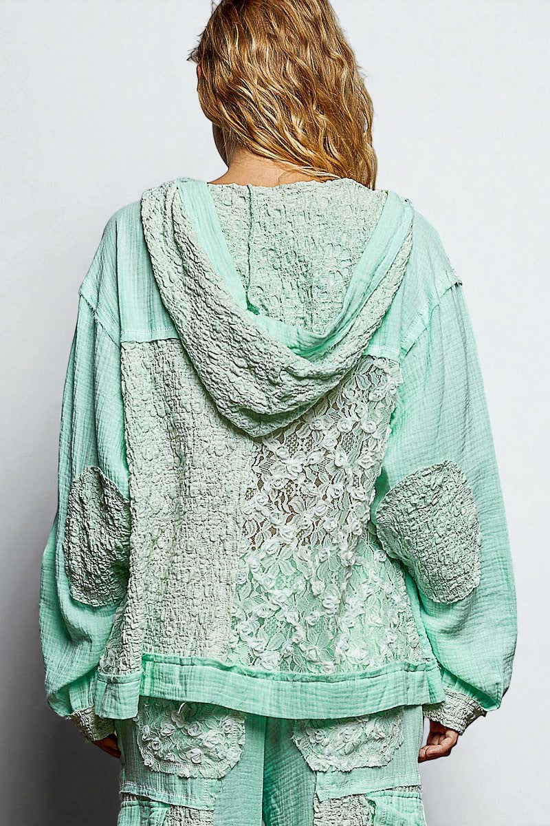 Person wearing a light green lace outfit with a hood on a plain background