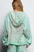 Person wearing a light green lace outfit with a hood on a plain background