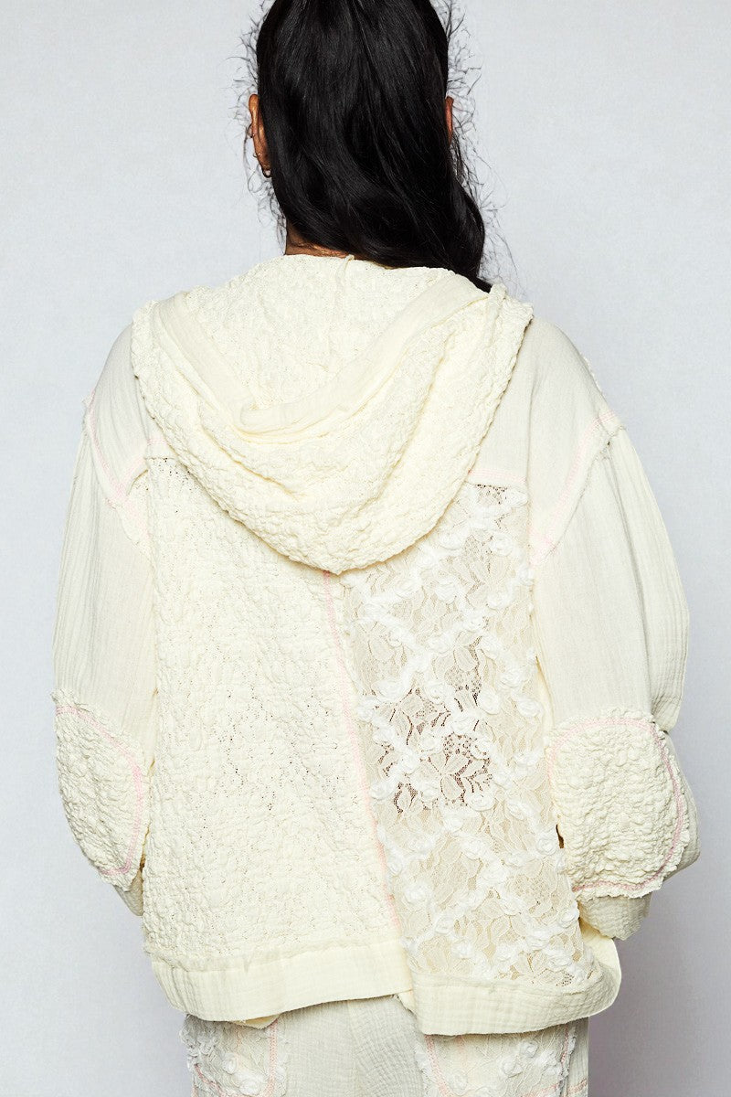 Person wearing a textured cream-colored hoodie with floral lace details on a plain background