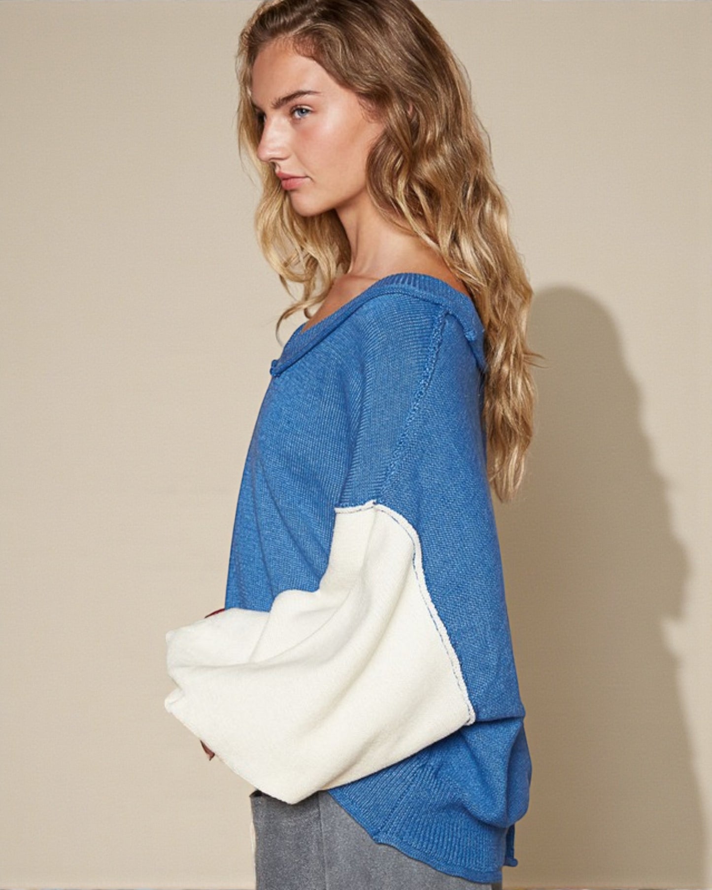 Woman wearing a blue sweater with white sleeves against a beige background