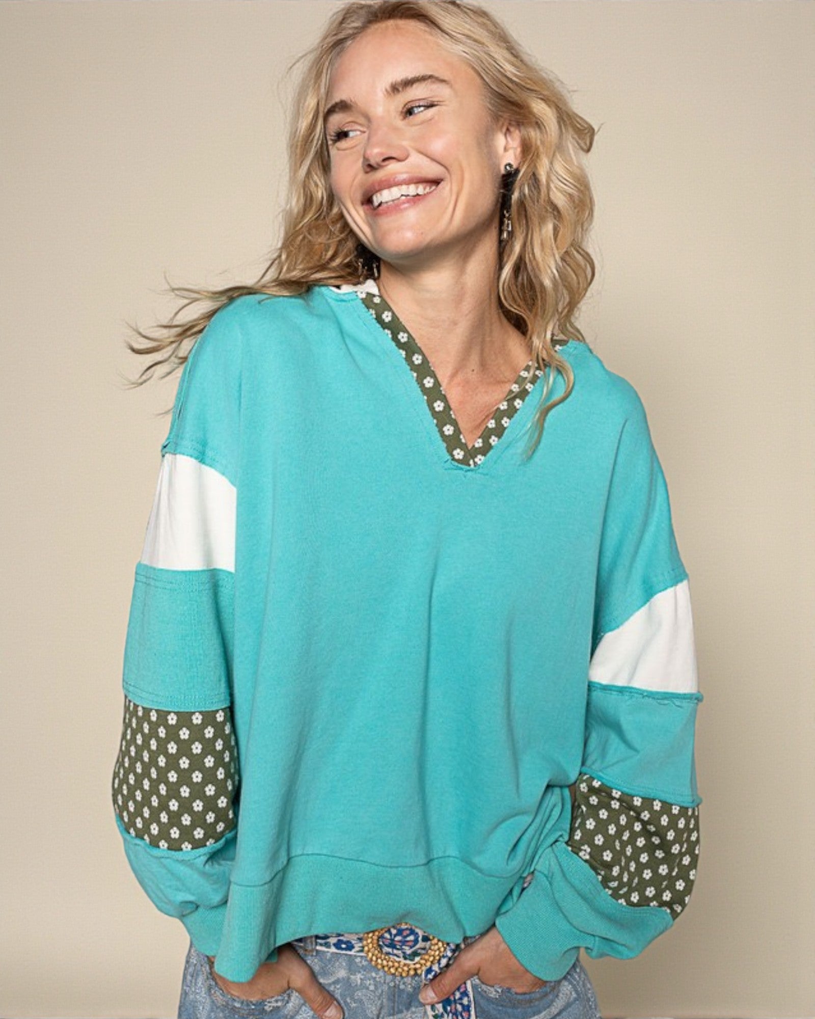 Woman wearing a turquoise sweater with polka dot cuffs and hem on a beige background