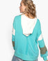 A woman shown from the back wearing a turquoise and white color-block hoodie with patterned elbow patches, against a plain white background.