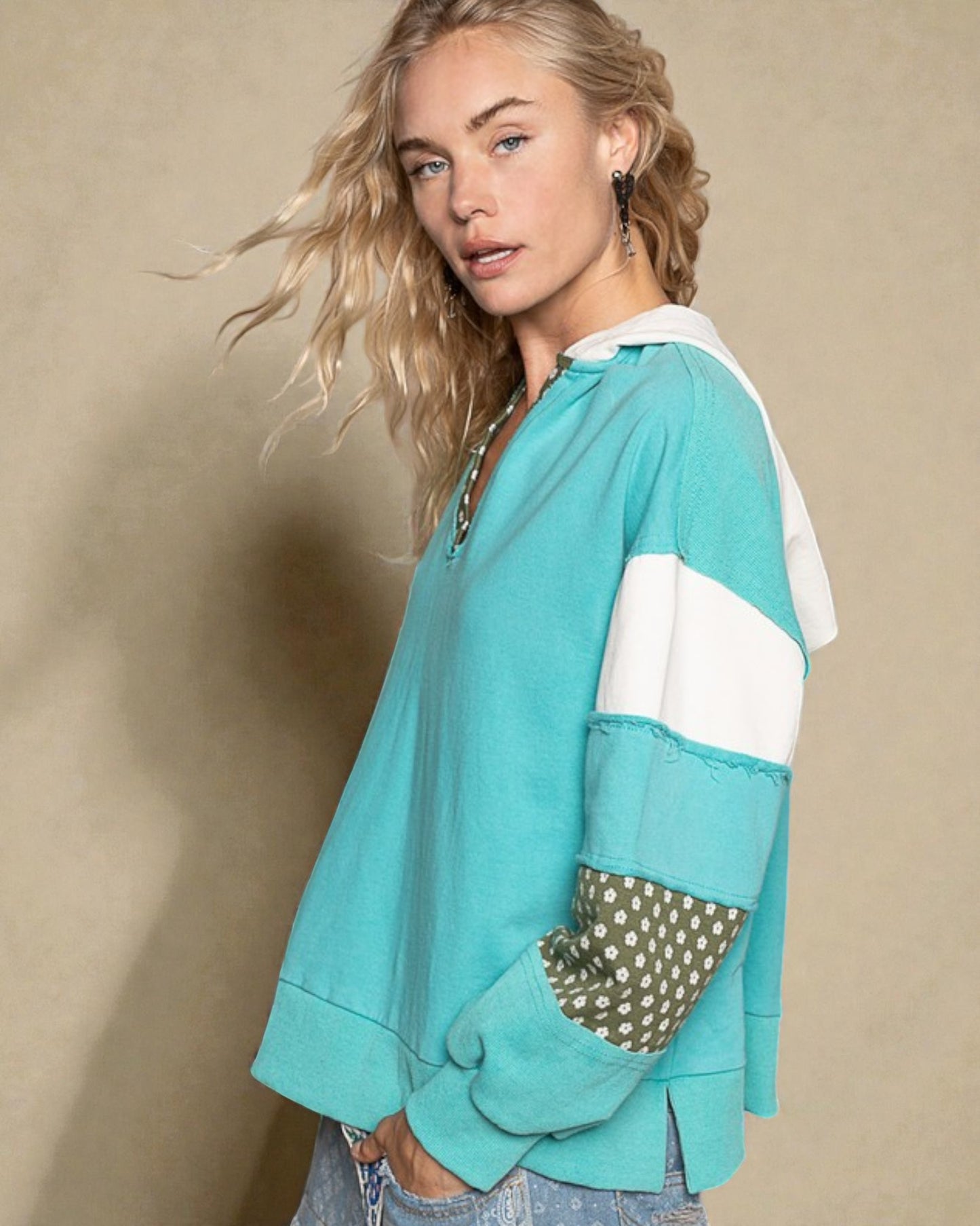 Woman wearing a teal sweater with white sleeves and polka dot cuffs against a beige background