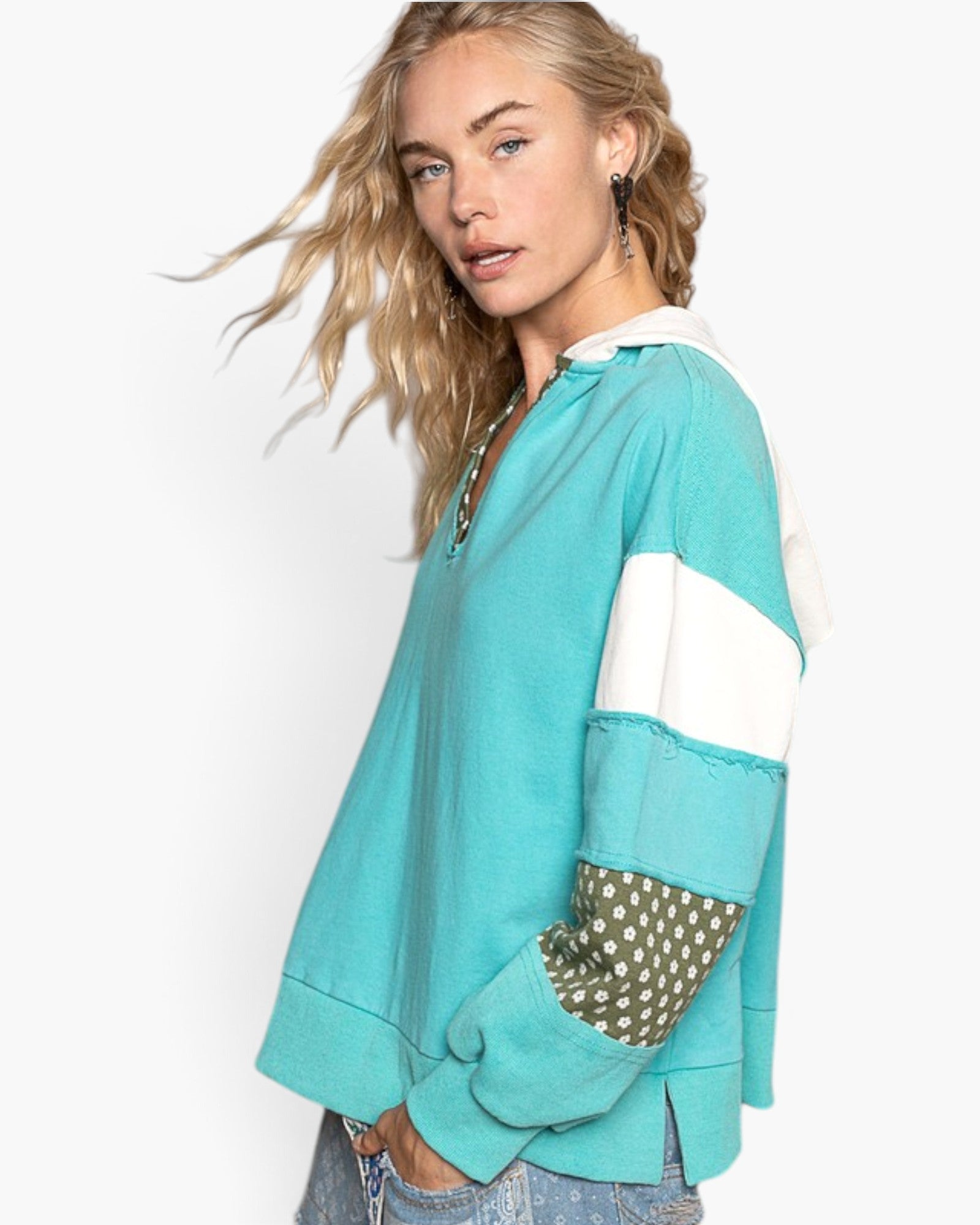 A woman wearing a turquoise and white color-blocked long-sleeve rugby shirt with olive green and white polka dot elbow patches, photographed against a clean white background.
