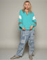 Woman wearing a teal sweater with white stripes and patterned pants on a plain background