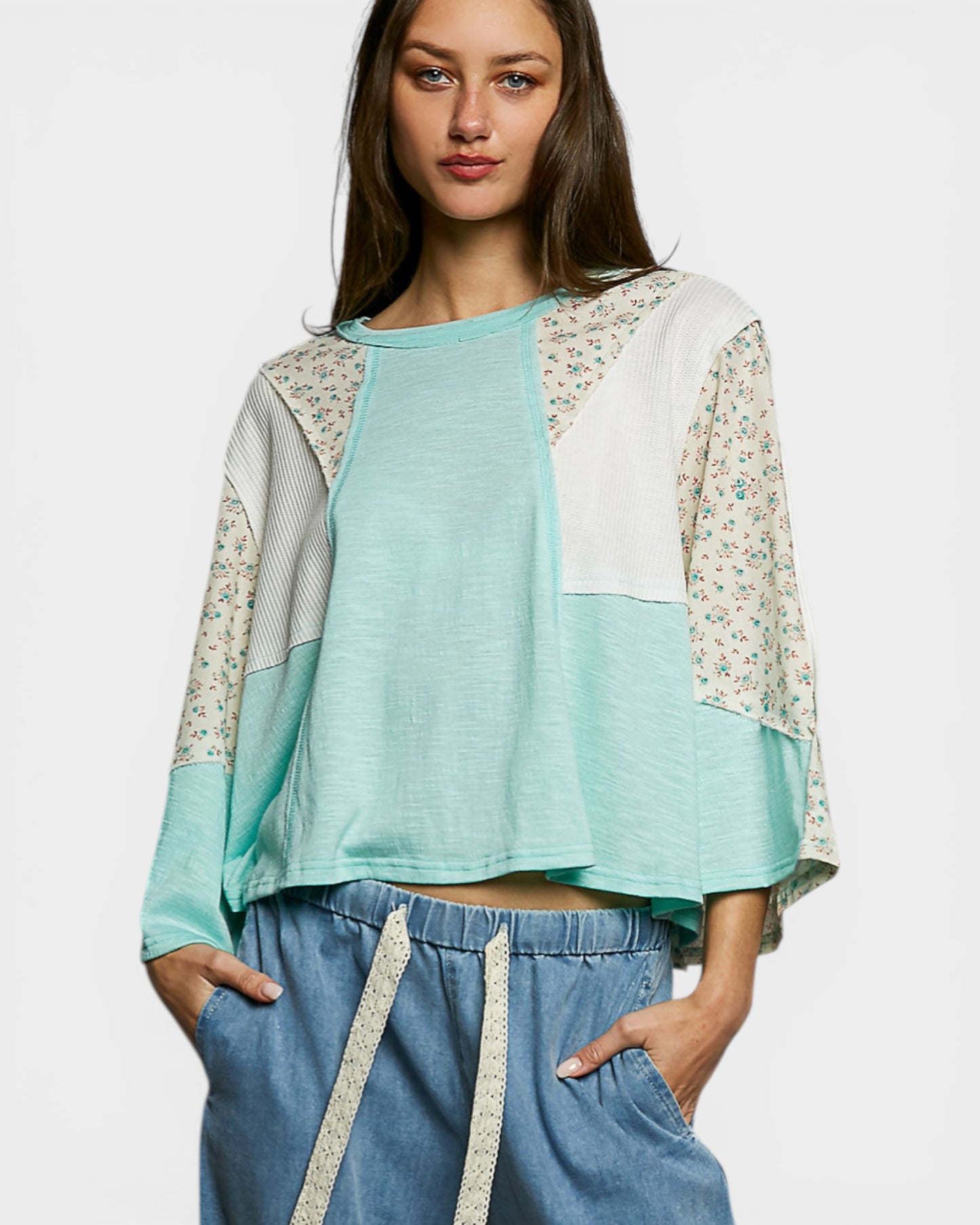Woman wearing a light blue top with floral sleeves and blue pants on a white background