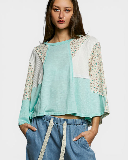 Woman wearing a light blue top with floral sleeves and blue pants on a white background