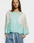 Woman wearing a light blue top with floral sleeves against a white background