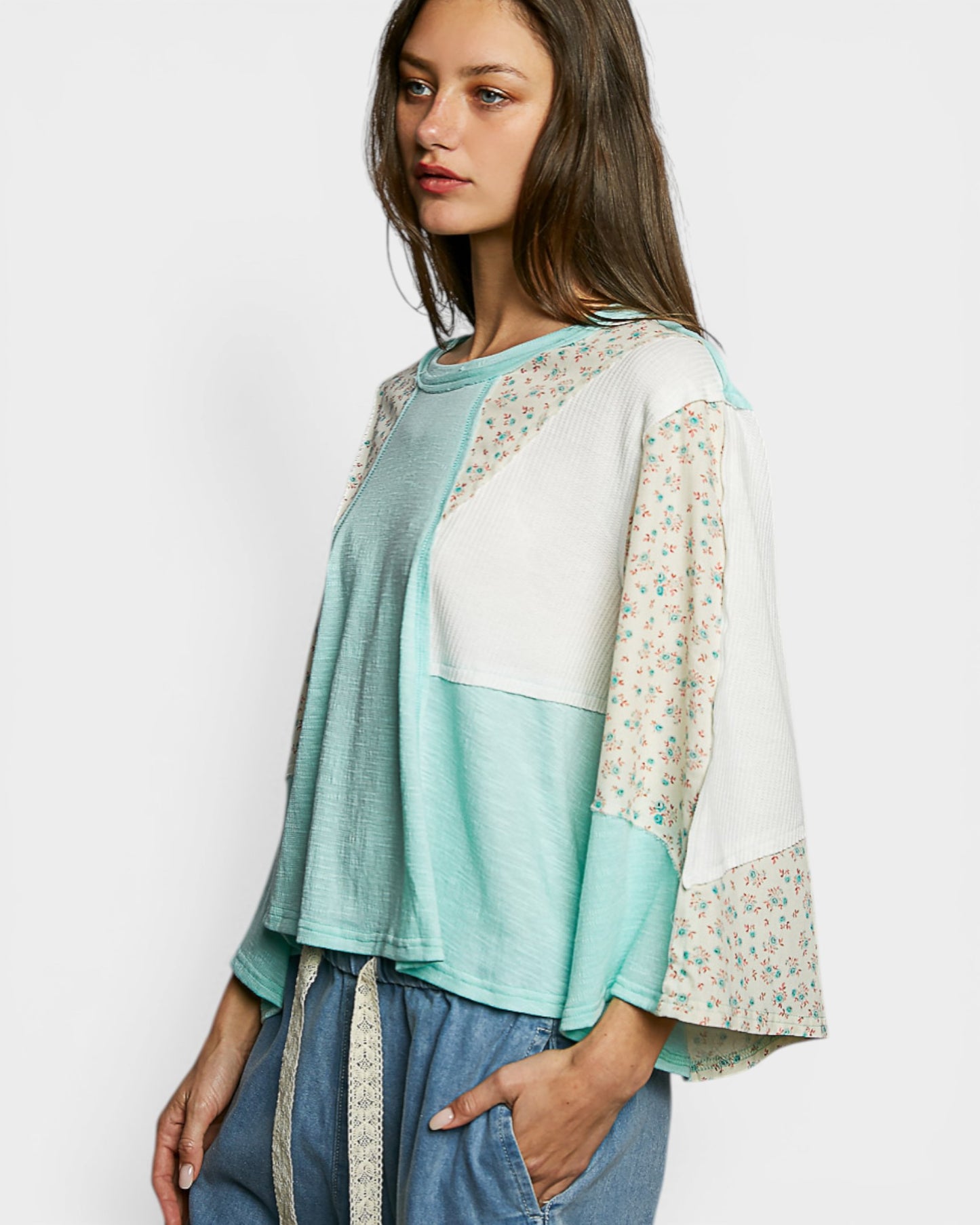 Woman wearing a light blue and white top with floral sleeves on a white background