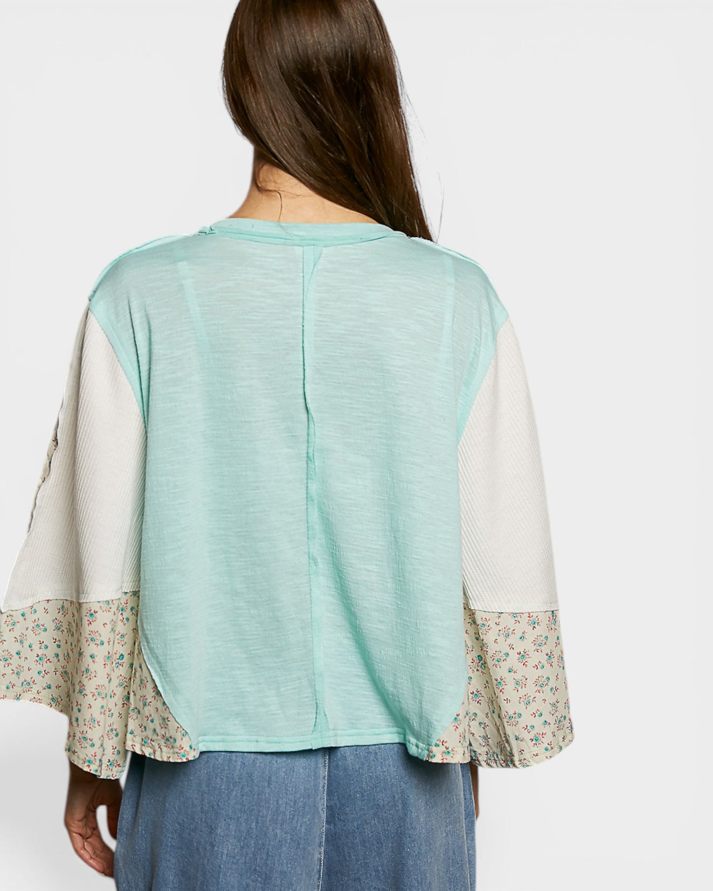 Back view of a person wearing a light green top with floral sleeves on a white background