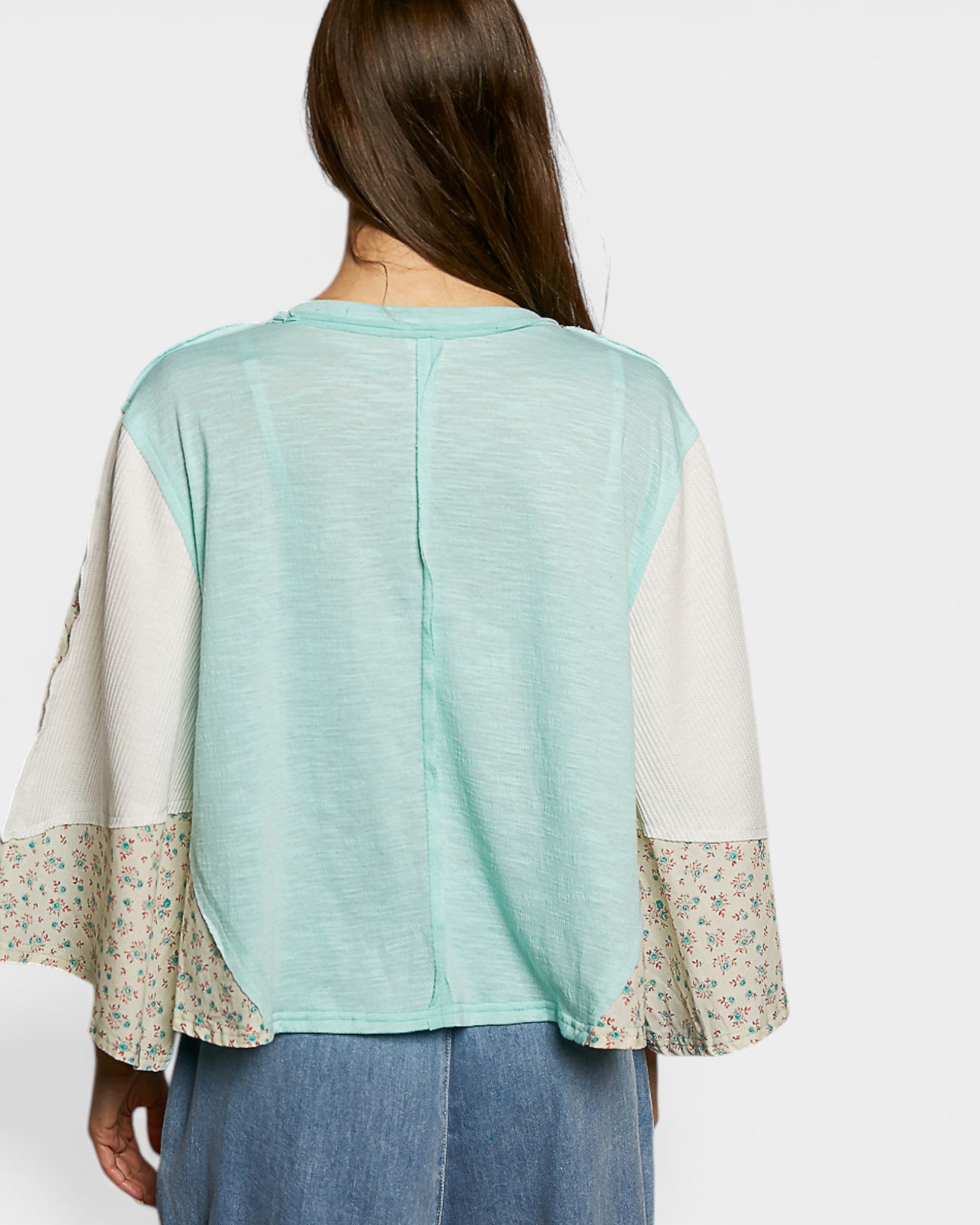 Back view of a person wearing a light green top with floral sleeves on a white background