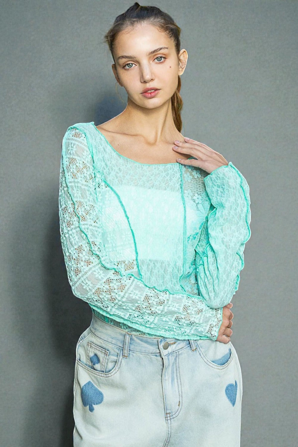 Woman wearing a light blue lace top and jeans against a gray background