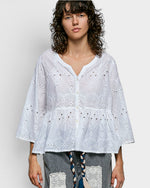 Woman wearing a light blue embroidered blouse against a plain background