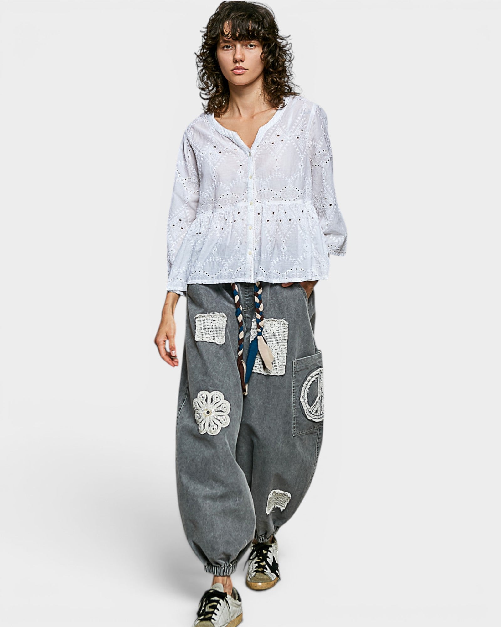 Person wearing a white blouse and gray patchwork pants on a white background