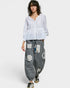 Person wearing a white blouse and gray patchwork pants on a white background