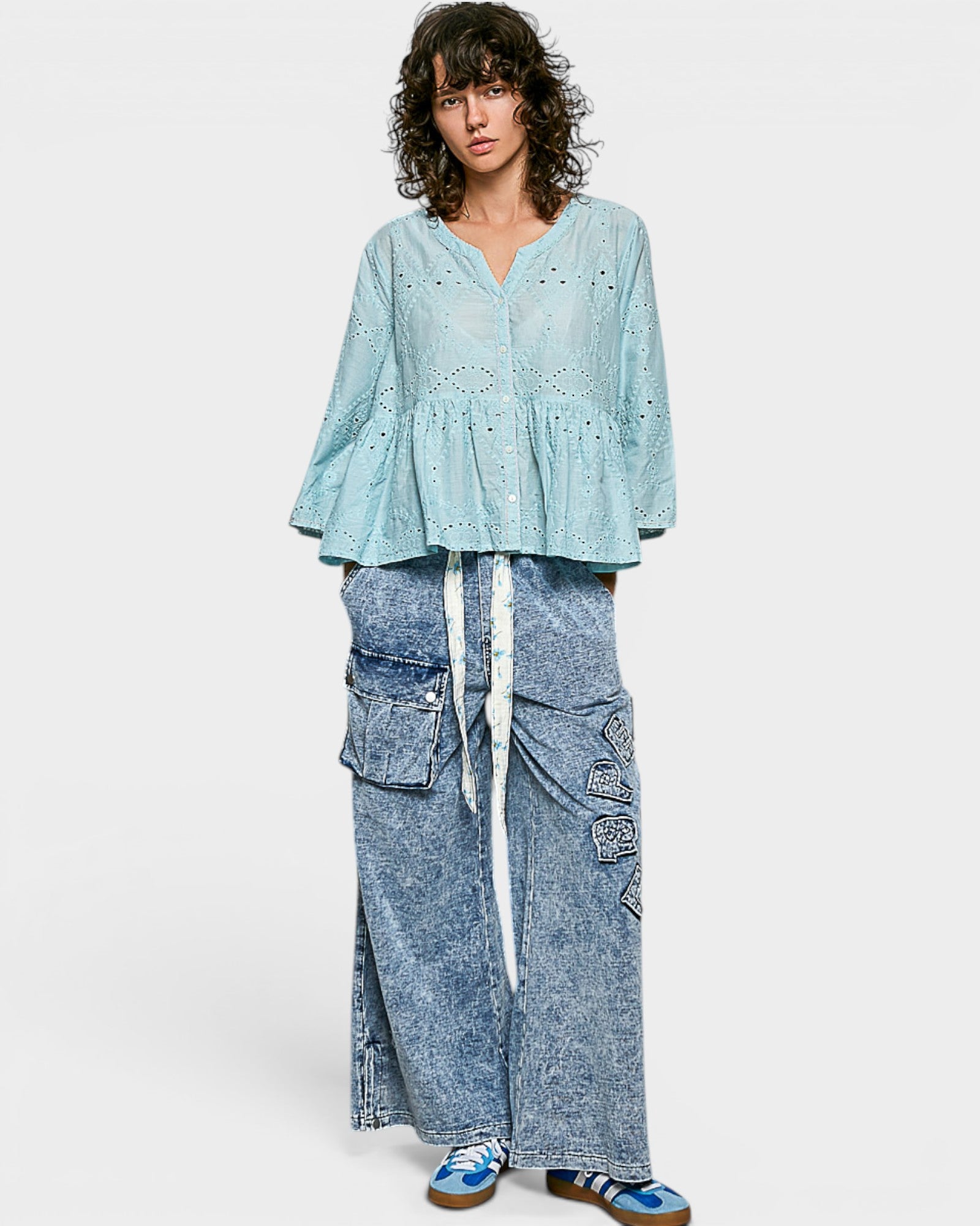 Woman wearing a light blue top and denim pants on a white background
