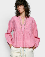 Woman wearing a pink embroidered blouse with a plain background