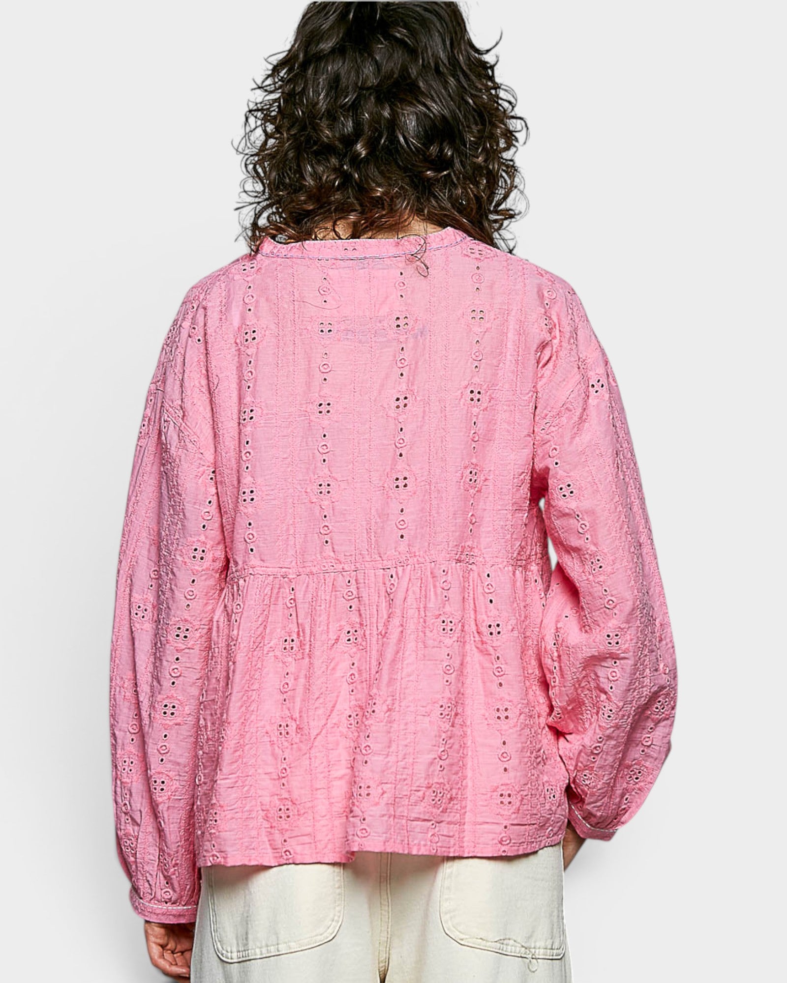 Person wearing a pink embroidered blouse with white pants on a light gray background