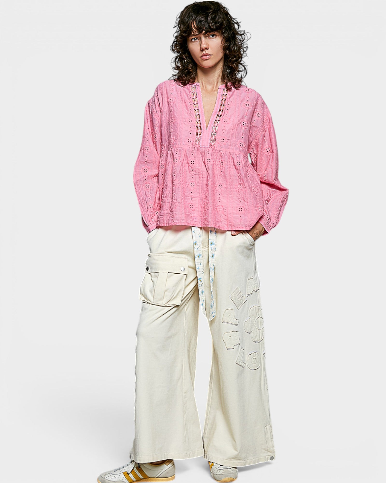 Person wearing a pink blouse and white pants on a plain background