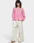 Person wearing a pink blouse and white pants on a plain background